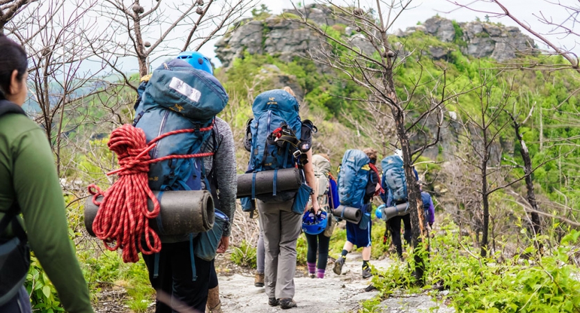 A group of backpackers hike along a trail in a wooded area. 