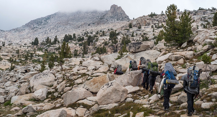 A group of backpackers hike over rocky terrain toward a mountain. 