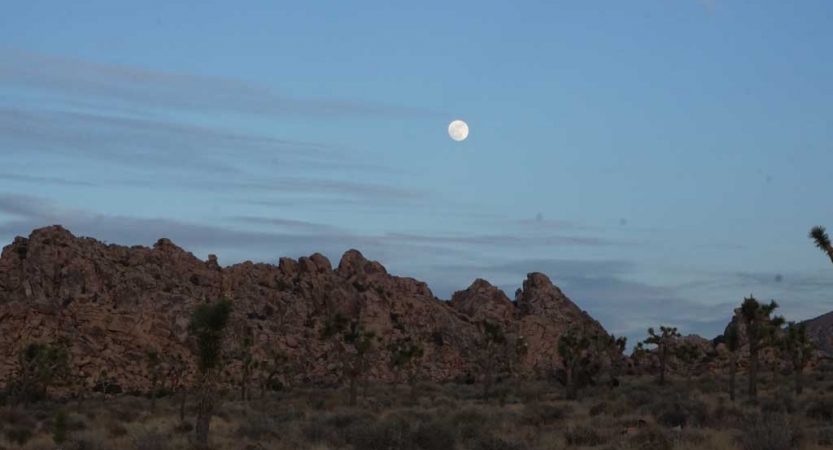 The moon shines in a darkened sky above a mountain landscape. 