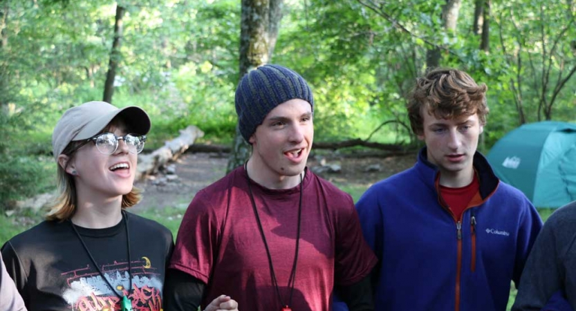 three students link arms in a wooded area