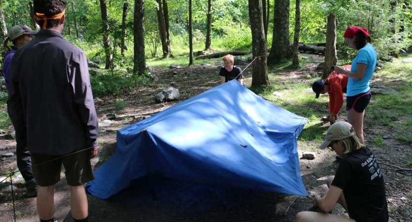 People work to set up a tarp shelter in a wooded area 