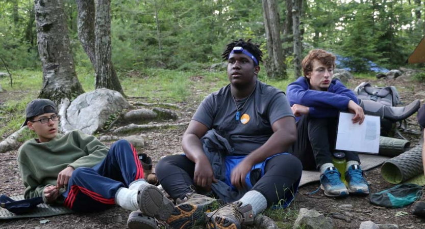 Three students rest in a wooded area. 