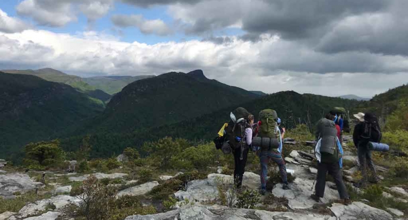 A group of people wearing backpacks hike along a rocky path in the blue ridge mountains. 