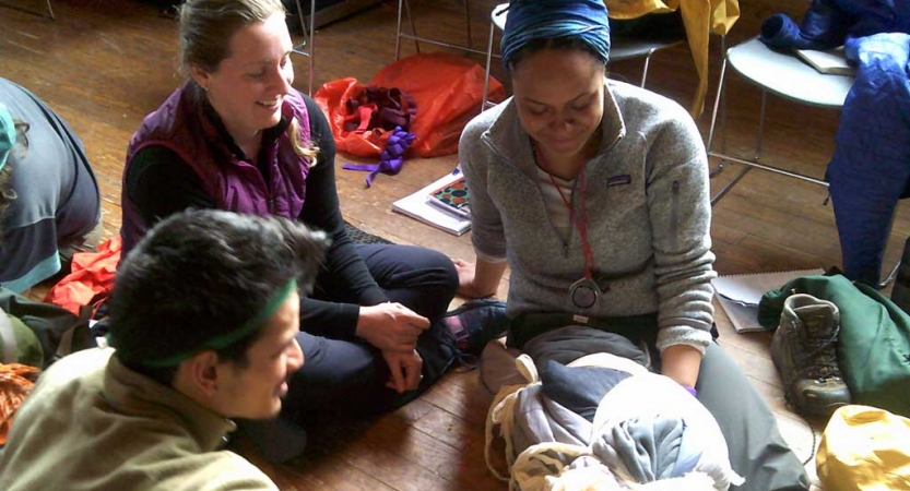 Three people sit in the floor, and on of them has their leg braced. They are taking part in a wilderness first responder certification. 