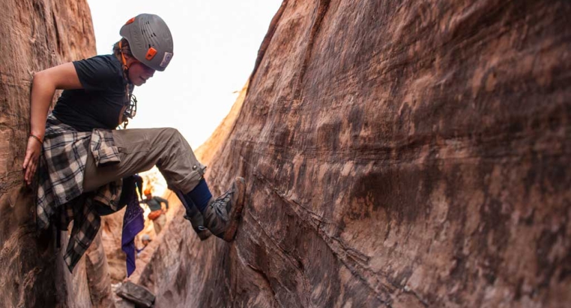 A person braces themselves on opposite walls of a slot canyon