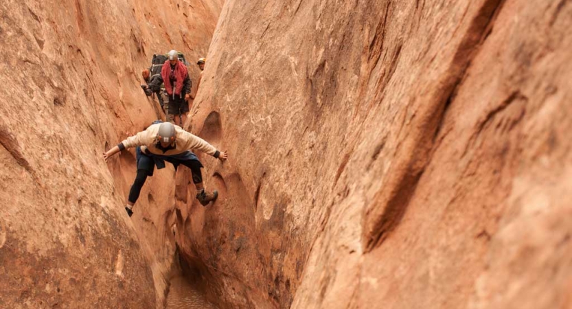 A person braces themselves on opposite walls of a slot canyon