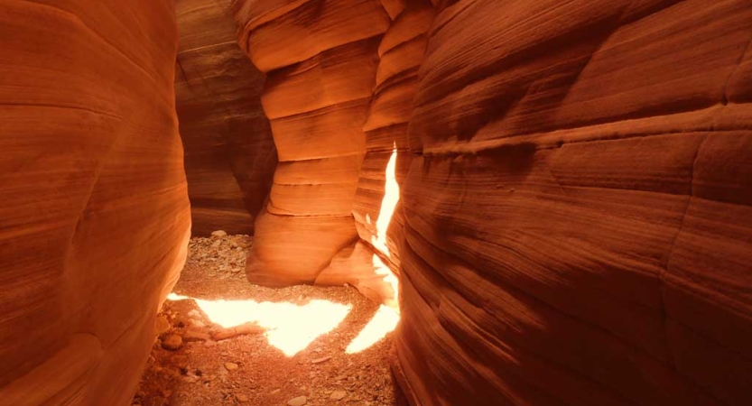 The sun shines through into a red slot canyon