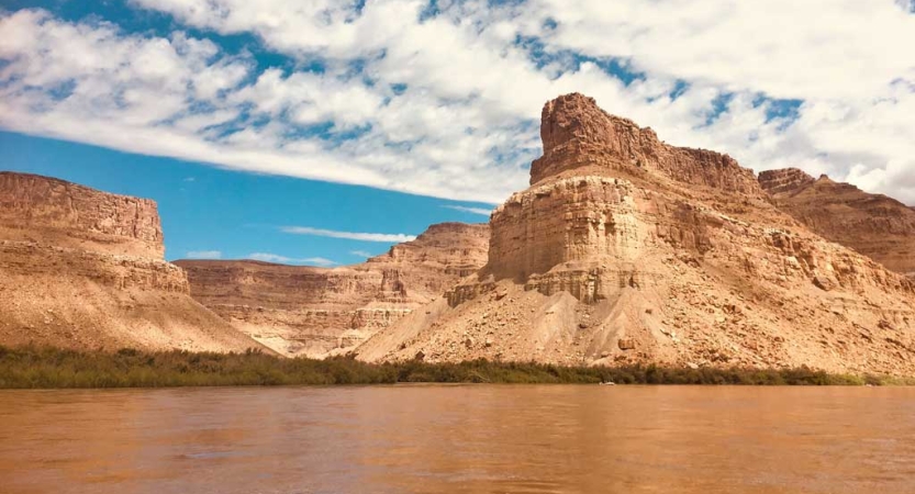 On the opposite shore of a body of water, tall rock formations reach toward the sky. 
