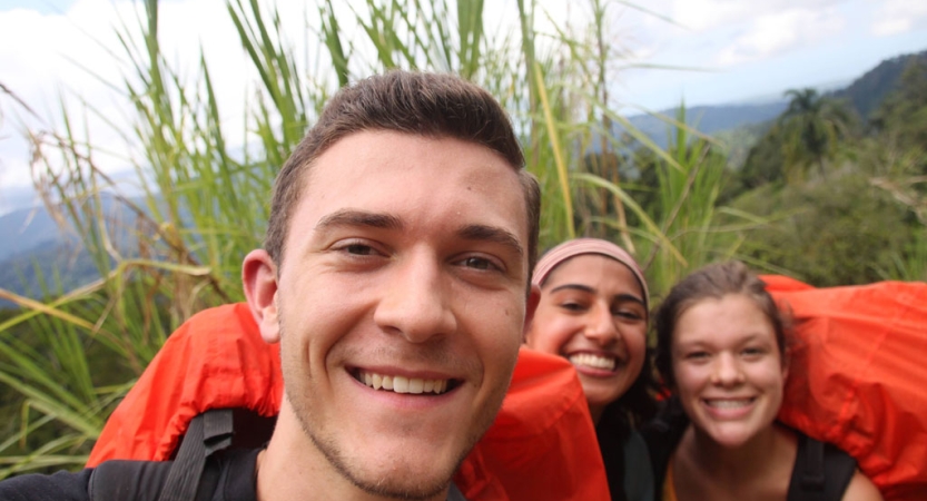Three people smile for a photo in front of greenery 