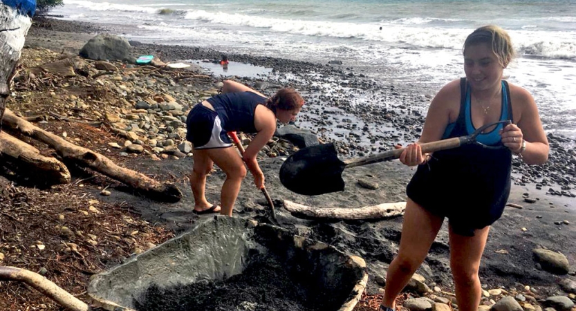 Two people use shovels during a service project on a beach. 
