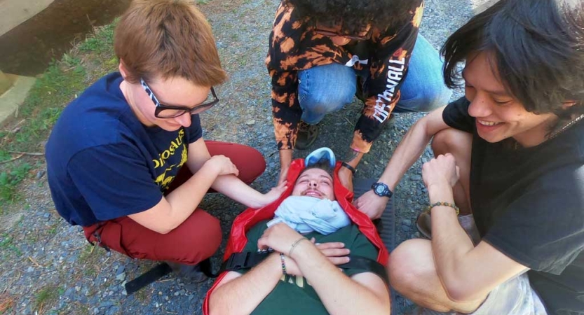 A person laying on the ground has their neck braced while three others are gathered around them. They are all participating in a wilderness first responder course. 