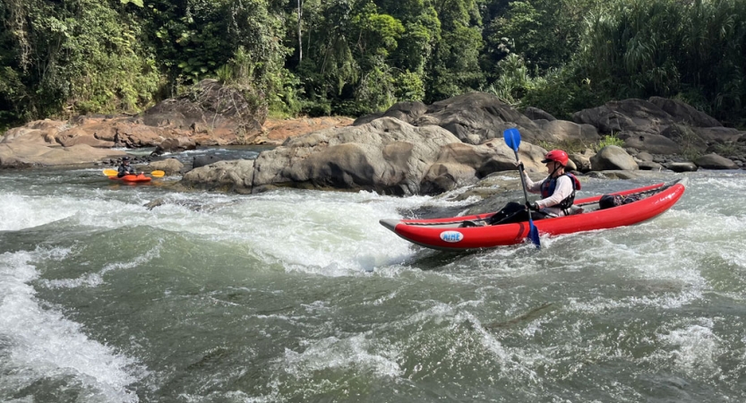 A person wearing safety gear paddles a watercraft through small rapids.