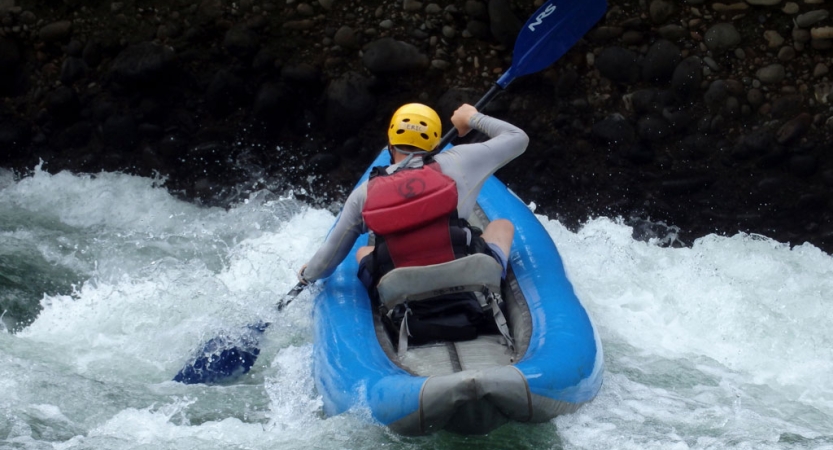 A person wearing safety gear paddles a watercraft through whitewater.
