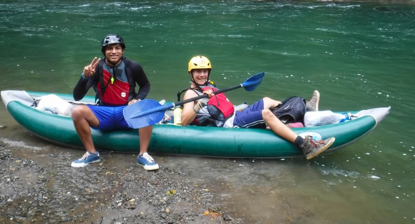 Two people wearing safety gear sit in a watercraft in shallow water.