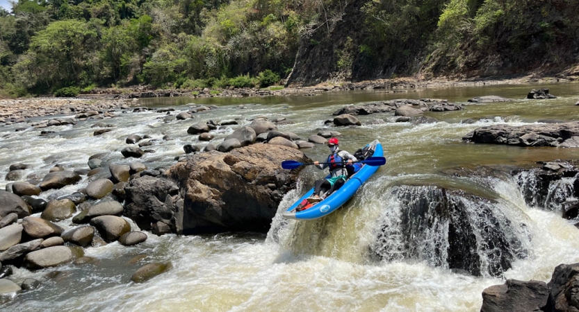 A person wearing safety gear paddles a watercraft over a small waterfall.