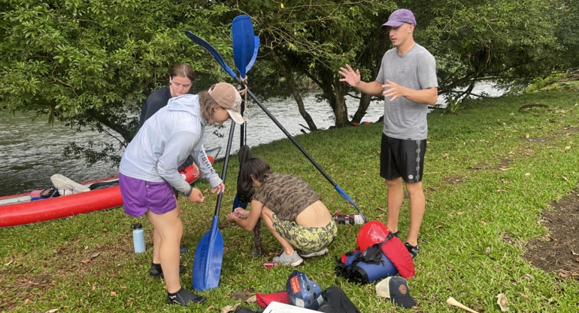 Four people use paddles during a training exercise on the shore.